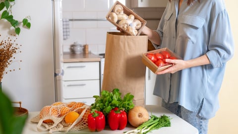 Woman at home getting groceries out of a shopping bag with grocery ordered from internet. Fresh organic vegetables, greens and fruits. Kitchen interior.  Food delivery concept; Shutterstock ID 2252672697