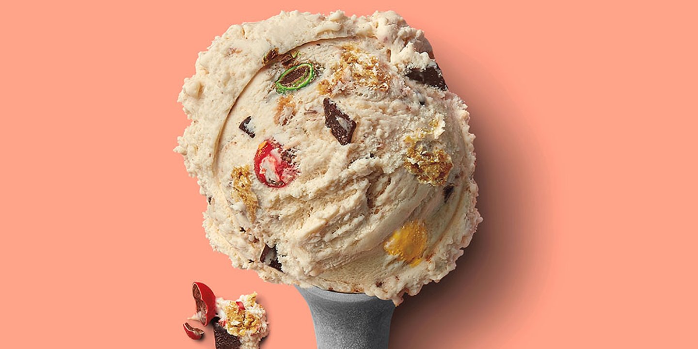 a heaping scoop of ice cream with visible pieces of m&ms, chocolate chunks and cookies on a salmon background