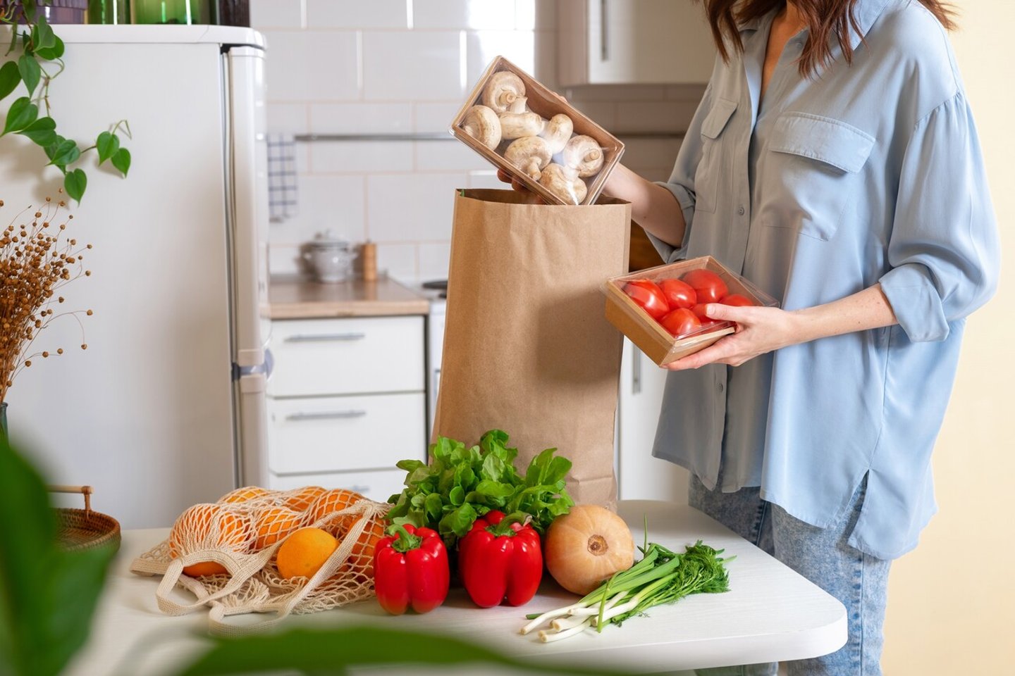 Woman at home getting groceries out of a shopping bag with grocery ordered from internet. Fresh organic vegetables, greens and fruits. Kitchen interior.  Food delivery concept; Shutterstock ID 2252672697