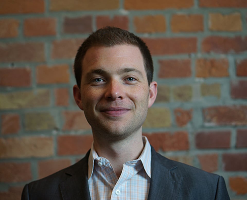 a man wearing a suit and tie standing in front of a brick wall