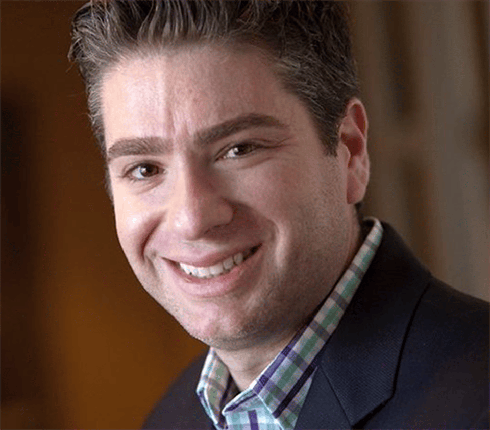 a man wearing a suit and tie smiling and looking at the camera