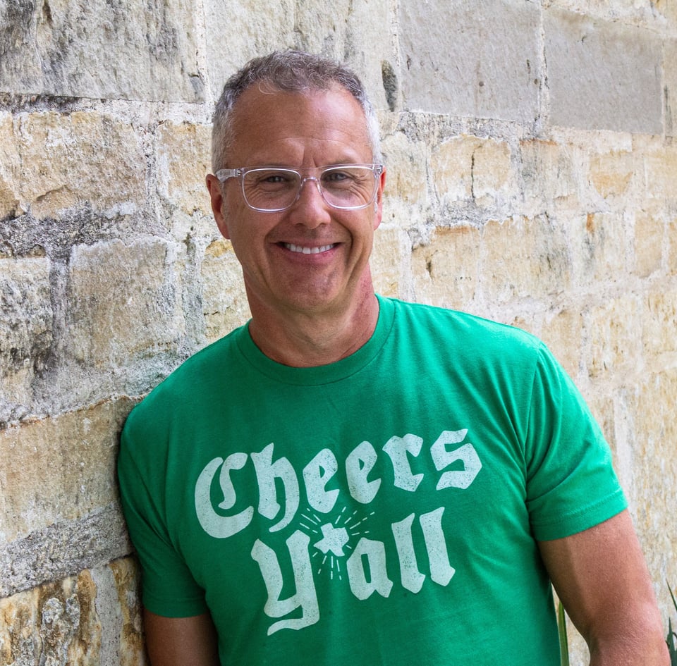 a smiling man in a green shirt standing in front of a building