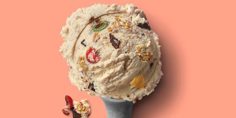 a heaping scoop of ice cream with visible pieces of m&ms, chocolate chunks and cookies on a salmon background