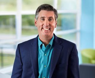 John Frinzi wearing a suit and tie smiling at the camera
